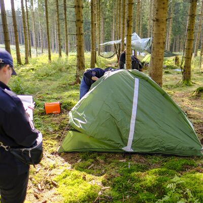 Bild vergr&ouml;&szlig;ern: Das Bild zeigt Personen, die sich ein Zelt im Wald ansehen.