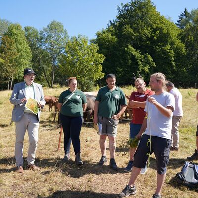 Bild vergr&ouml;&szlig;ern: Das Bild zeigt eine Gruppe von Menschen, die einem Vortrag auf einer Wiese zuh�ren.
