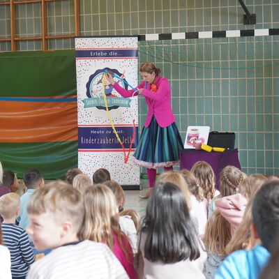 Bild vergr&ouml;&szlig;ern: Das Bild zeigt viele Kinder, die gespannt einer Zauberin zuschauen.